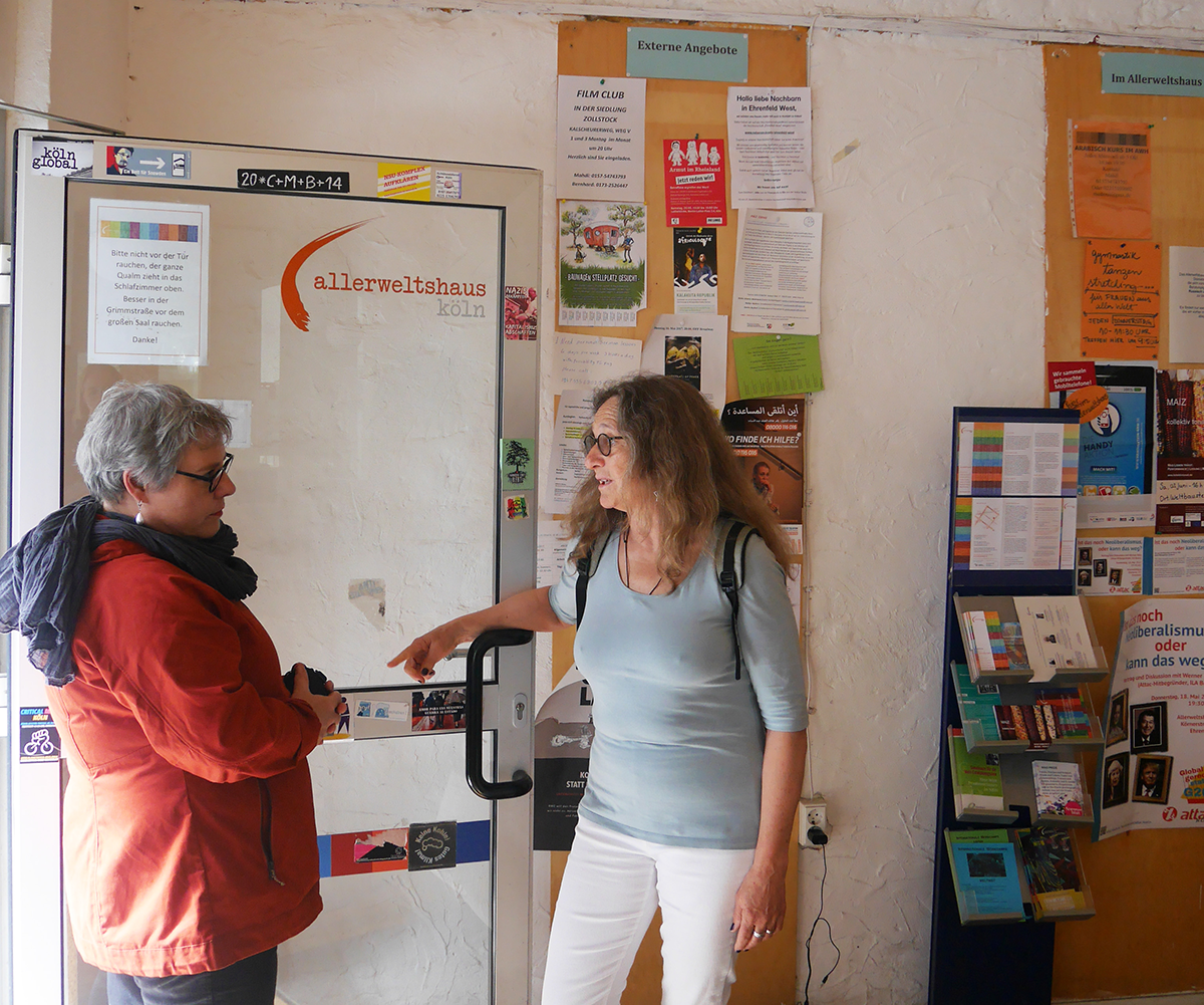 Michaela Pfaff und Anne Kuhlmann stehen bei geöffneter Tür im Eingang des Allerweltshauses in Köln-Ehrenfeld und sprechen miteinander (Julia Hitschfeld/Caritas)