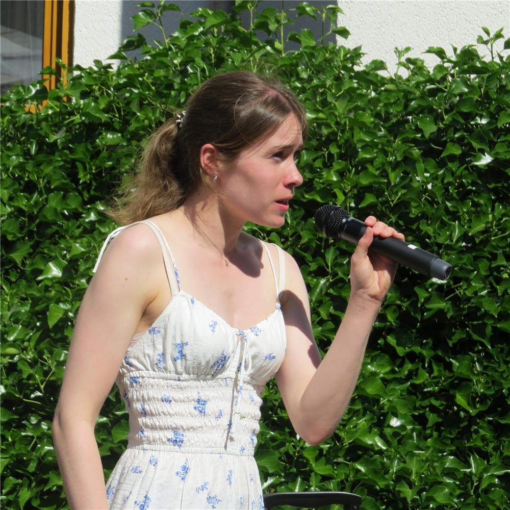Sängerin mit Mikrofon vor einer Hecke 