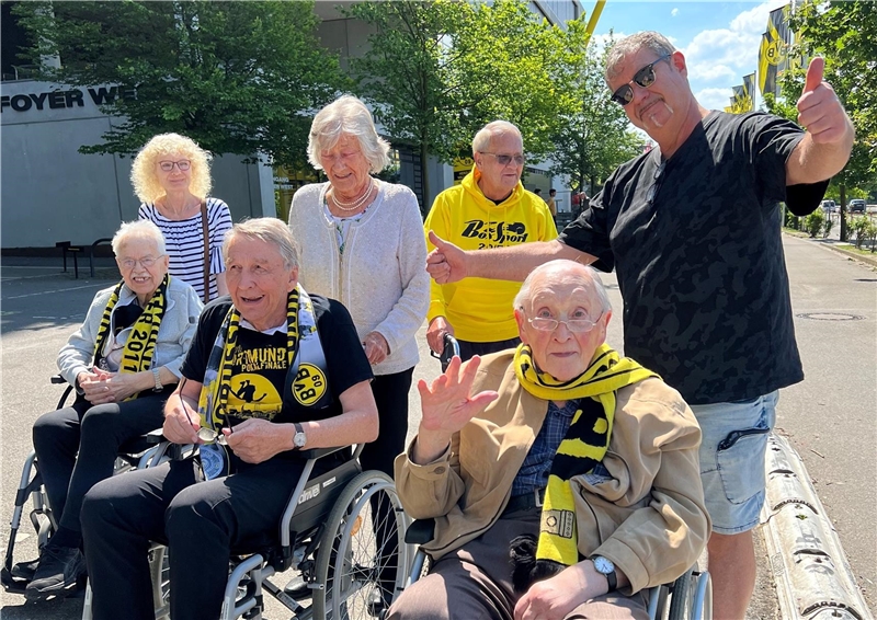 Eine Gruppe Menschen, teilweise im Rollstuhl, trägt BvB Schals und Kleidung