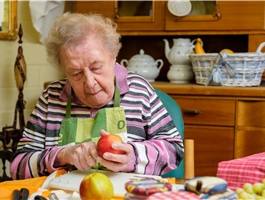 Eine Seniorin sitzt an einem Tisch und schält einen Apfel / Werner Krüper