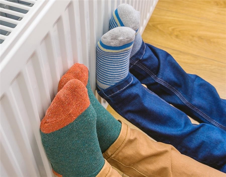 Zwei Kinder wärmen sich mit bunten selbstgestrickten Socken die Füße an einem Heizkörper.