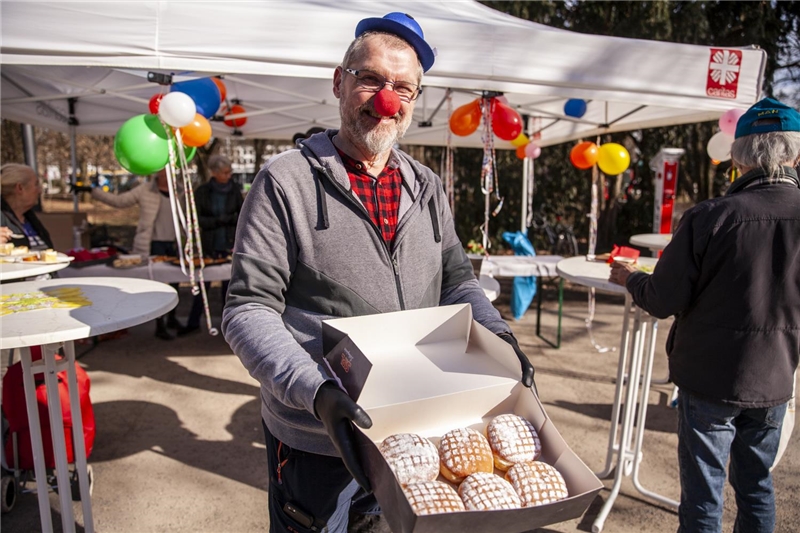 Christian Hierold steht vor der Veranstaltung mit vielen Krapfen in den Händen und als Clown verkleidet.