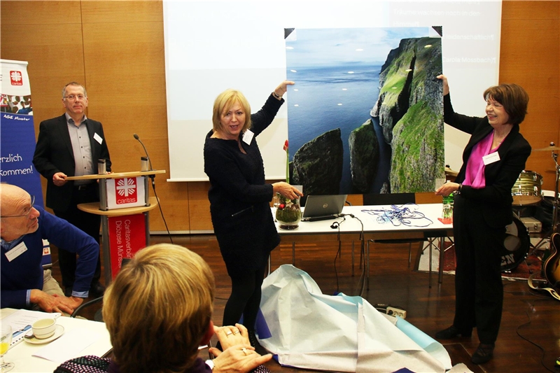 Zwei Frauen halten ein großes Landschaftsbild hoch.