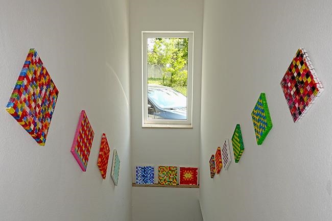 Ein Treppenabgang mit 13 quadratischen, schachbrettartigen Bildern an den Wänden (Caritasverband Darmstadt e. V. / Jens Berger)