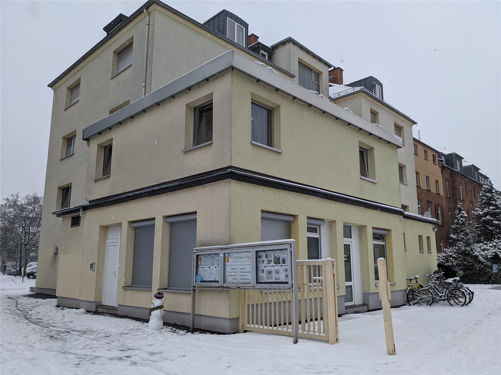 Ein kleiner Schneemann steht vor dem verschneiten Franziskus-Haus.