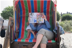 Mutter und Kind sitzen im Strandkorb und lesen eine Zeitschrift