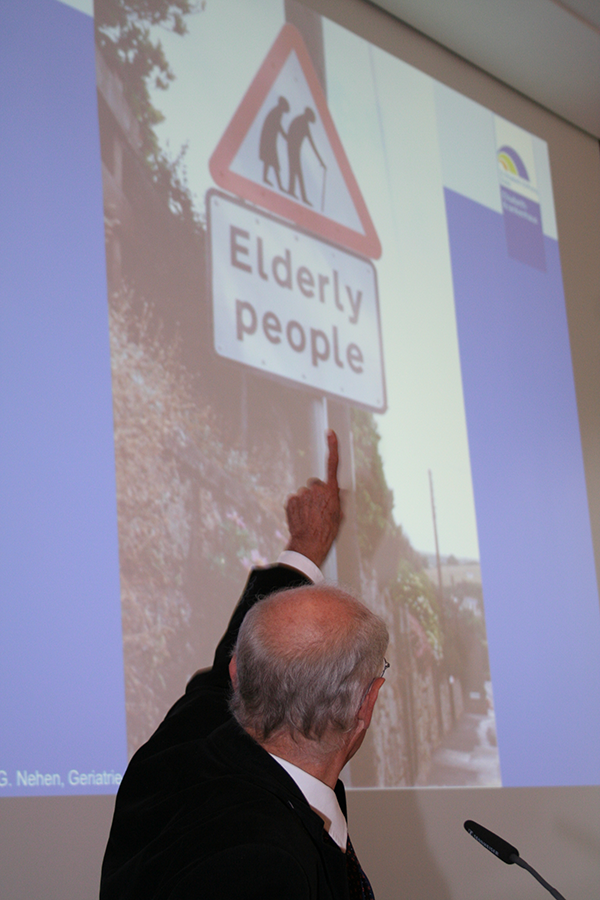 Prof. Dr. med. Hans Georg Nehen steht vor einem Rednerpult und deutet mit dem linken Zeigefinger umgewandt auf ein, auf einer Leinwand dargestelltes Bild. (Markus Lahrmann)