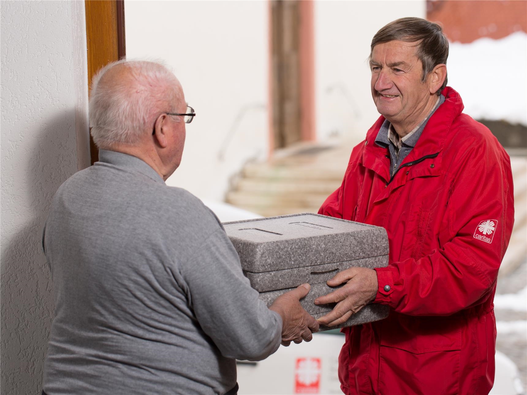 Caritasmitarbeiter bringt älterem Mann Essensbox