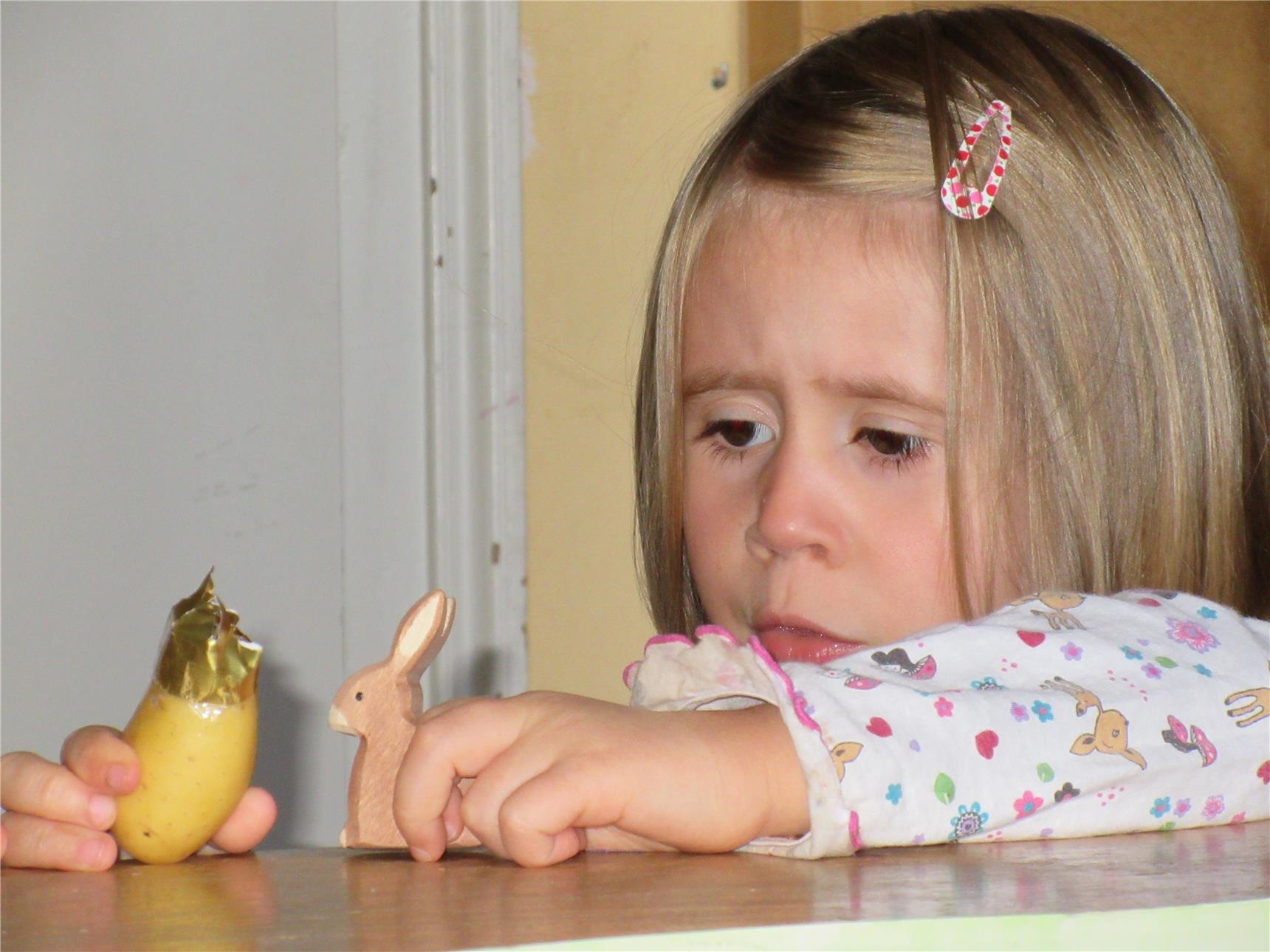 Ein Mädchen spielt auf einem Tisch mit zwei Figuren, einem Häschen und einer Kartoffel mit Papierkrone (Caritasverband Trier e. V.)