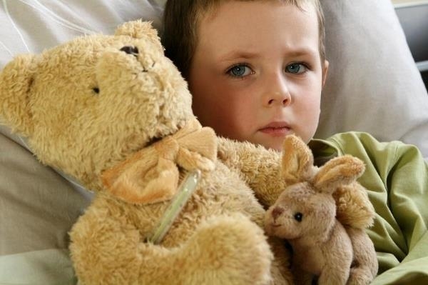 Kranker Junge im Bett liegend mit  Teddy im Arm
