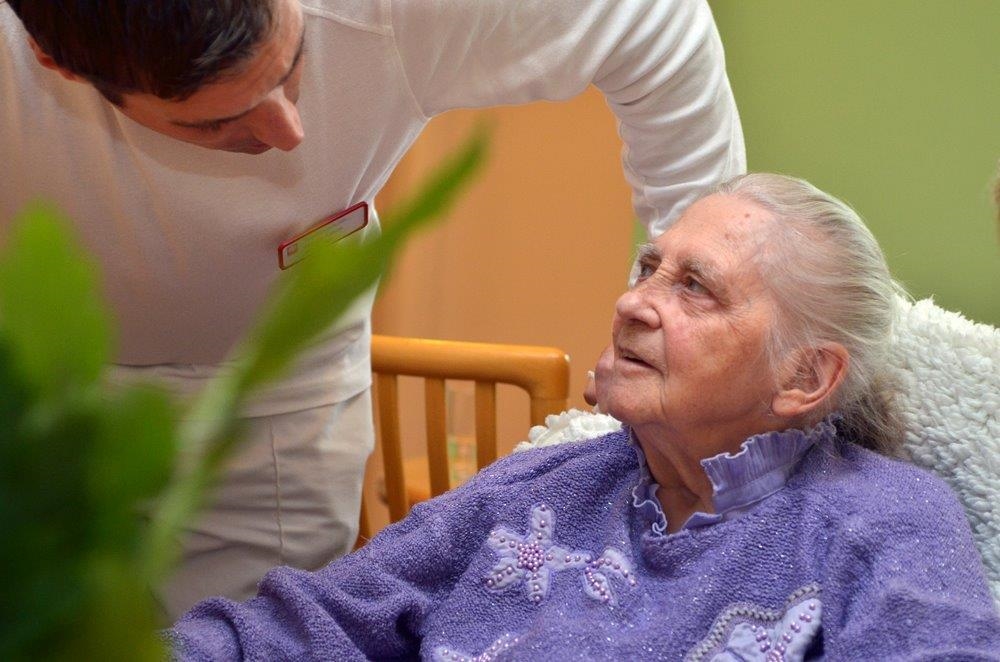 Pfleger beut sich über Seniorin, die ihn anlächelt (Tobias Schneider, taylormade)