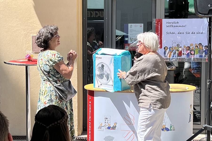 Eine Frau überreicht einer anderen Frau einen Bodenventilator als Geschenk (Caritasverband Darmstadt e. V. / Jens Berger)