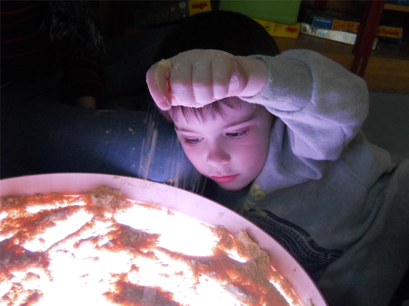: Ein Kind schaut auf die von unten beleuchtete durchscheinende Platte eines Tischs, auf der Maismehl verteilt ist (Caritasverband Trier e.V.)