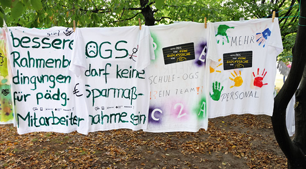 Vier weiße T-Shirts die anlässlich der OGS-Kampagne der LAG FW NRW bedruckt bzw. bemalt und an Wäscheleinen zwischen Bäumen auf der Landtagswiese aufgehängt wurden (Markus Lahrmann)