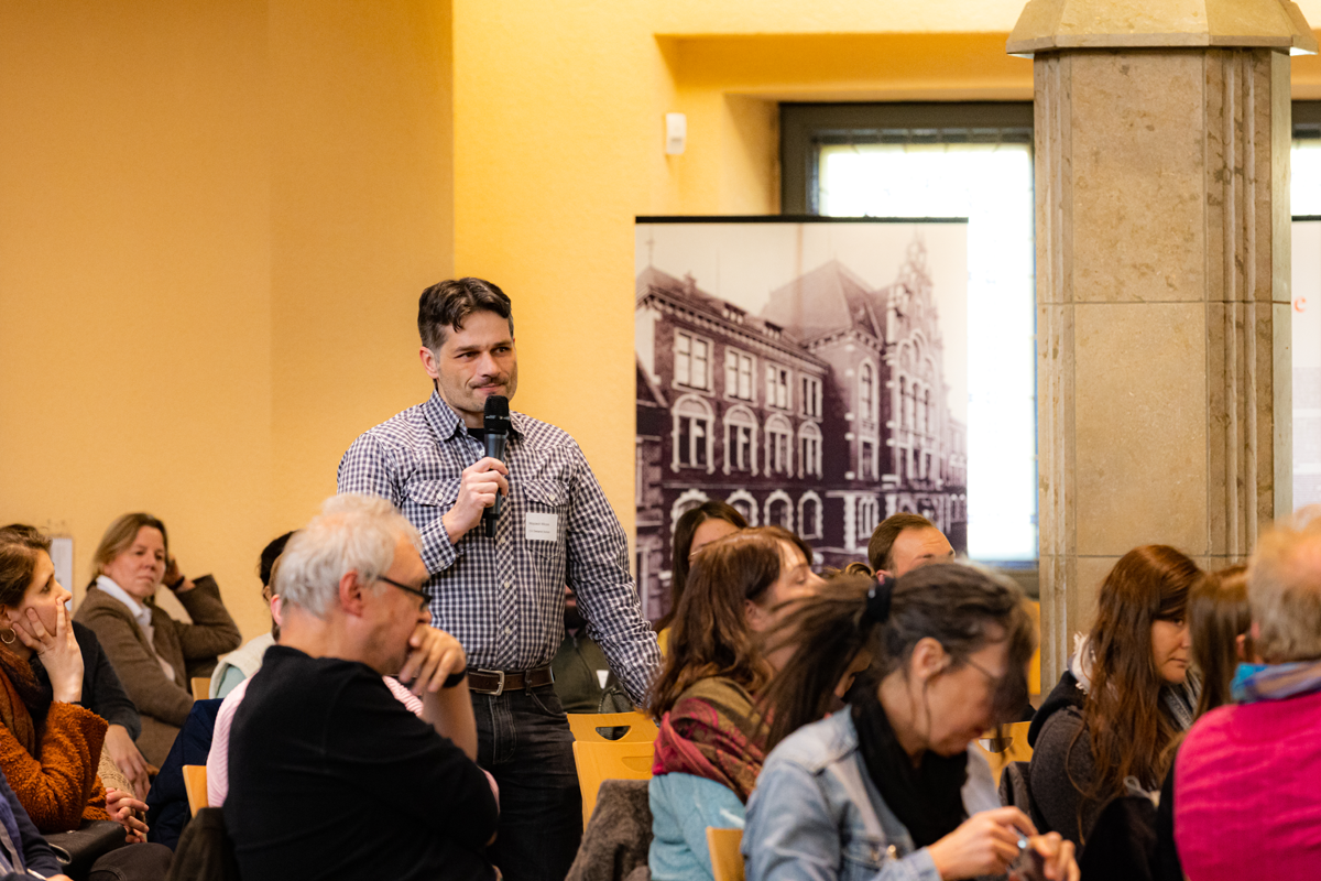 Ein Teilnehmer der der CiNW-Fachtagung 'Miteinander Gegeneinander?' in der Alten Synagoge in Essen steht im Publikum und stellt eine Frage (Foto: © Angelika Kamlage | Caritas in NRW)
