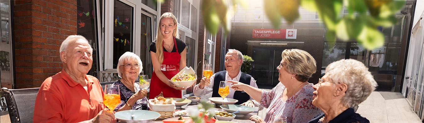 Senior:innen beim gemeinsamen Essen auf einer hellen Terrasse.