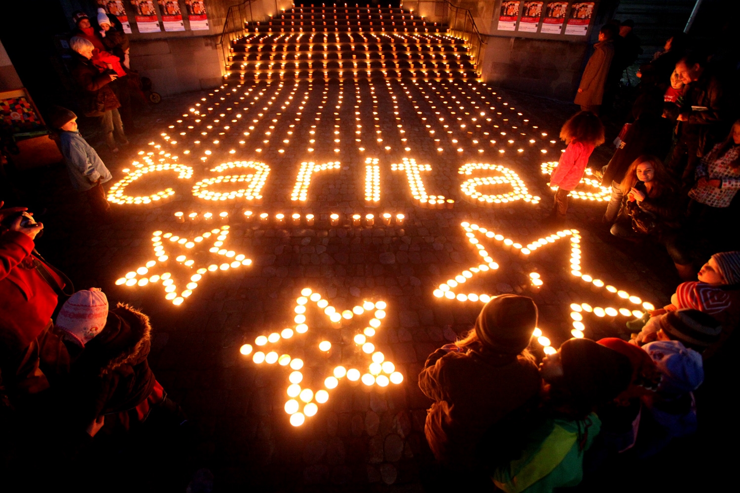 Brennende Kerzen im Dunkeln bilden den Schriftzug "Caritas"