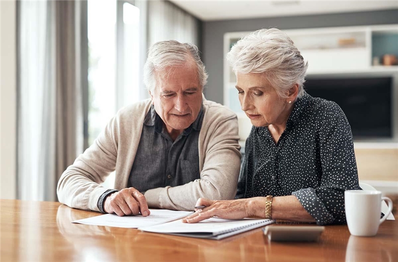 Älteres Ehepaar beugt sich über ein Dokument und berät sich.