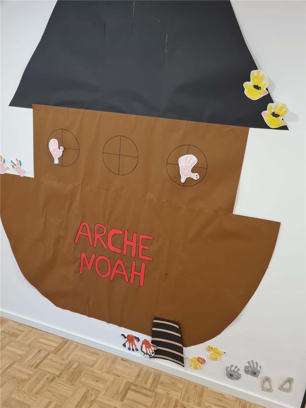 Eine aus bunter Pappe gebastelte Arche Noah klebt an einer Wand. 