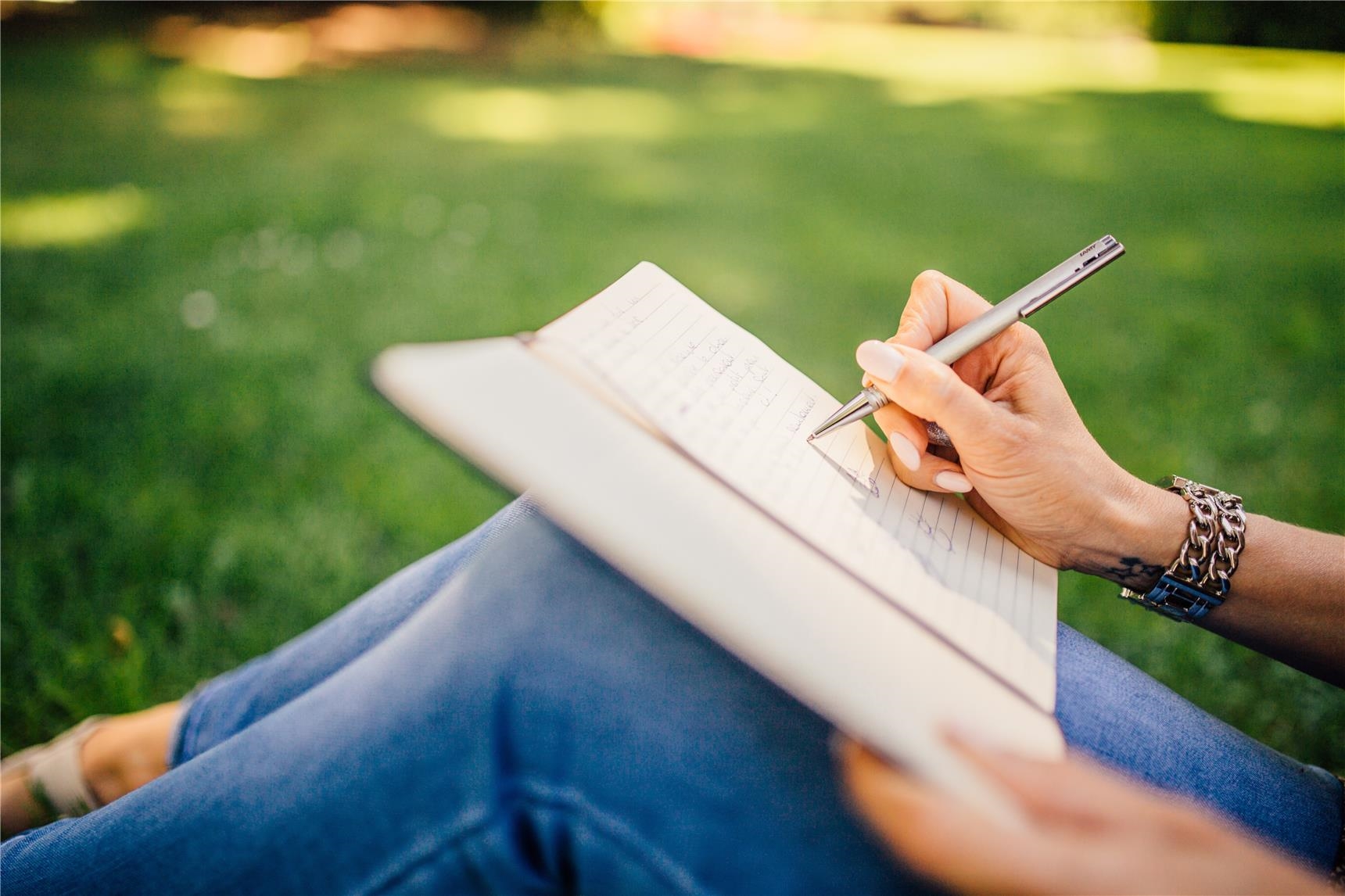 Eine Frau sitzt auf einer Wiese und schreibt etwas in ein Notizbuch