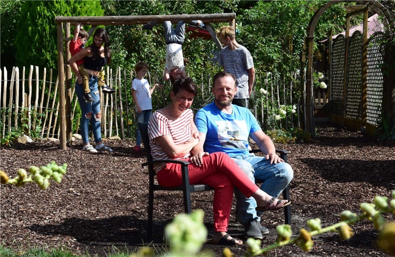 Eine Pflegefamilie aus Oberhausen sitzt in ihrem Garten, ihre Kinder spielen im Hintergrund.