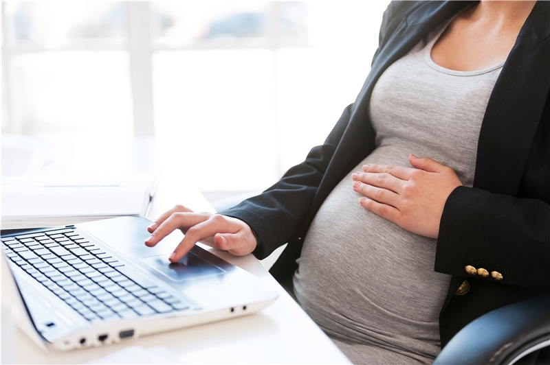Beschnittenes Bild einer schwangeren Geschäftsfrau, die etwas auf dem Laptop tippt, während sie an ihrem Arbeitsplatz im Büro sitzt