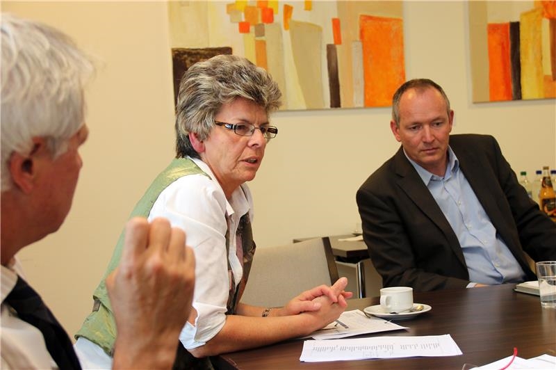 Das Foto zeigt eine Frau, die spricht und daneben einen Mann an einem Tisch sitzend.