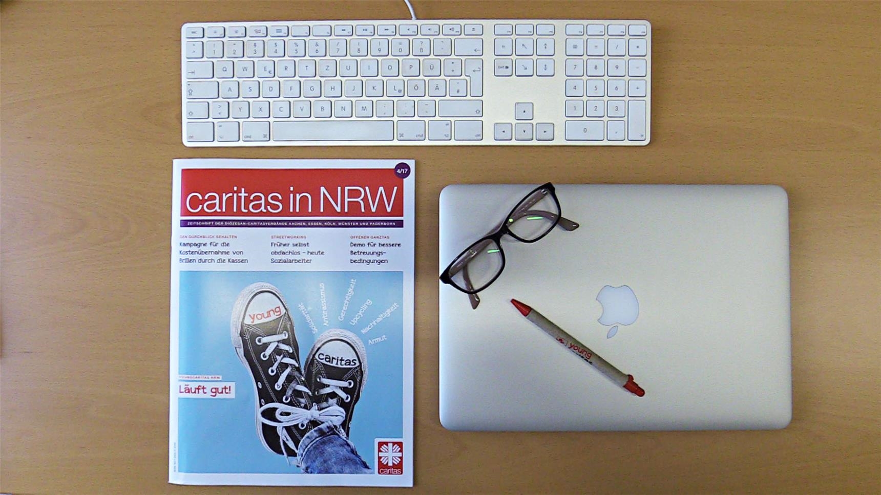 Auf einem Schreibtisch liegen die Zeitschrift "caritas in NRW", ein Laptop und eine Tastatur.