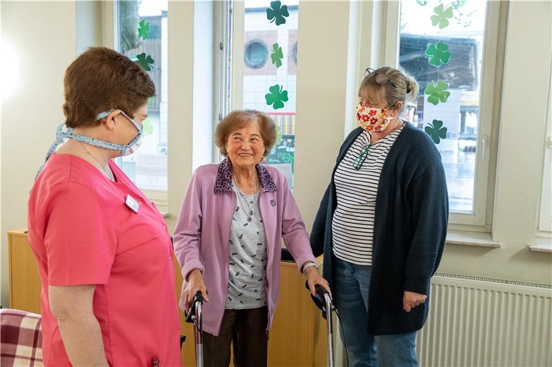 Das Foto zeigt eine Altenheim-Bewohnerin im Gespräch mit zwei Betreuuerinnen.