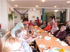 An einer langen Tafel sitzen Senioren bei Kaffe und Kuchen. Sie werden von einer Schwester bedient.