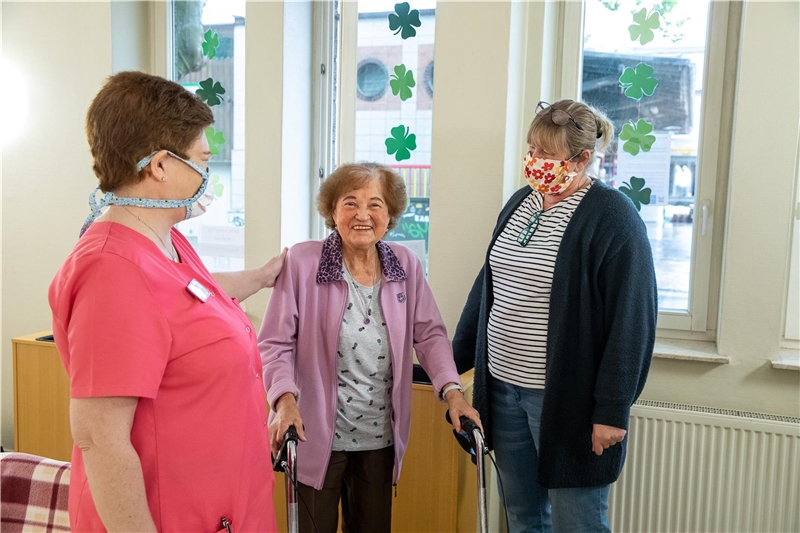 Das Foto zeigt zwei Altenpflegerinnen mit Mundschutz mit einer alten Frau mit Rollator.