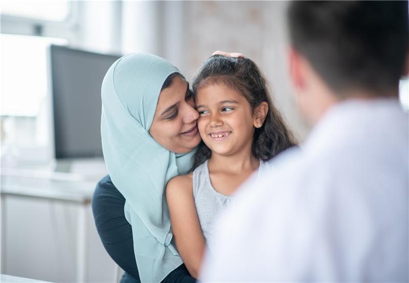 Eine muslimische Mutter und Tochter sind zusammen in ihrer Arztpraxis für eine Untersuchung. Sie umarmen sich liebevoll.