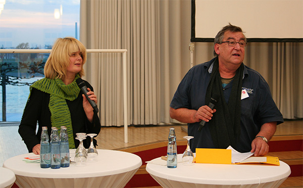 Die Projektkoordinatorin Nicola Buskotte und ein weiterer Redner stehen mit Handmikrofonen neben zwei Stehtischen auf dem Podium (Markus Lahrmann)