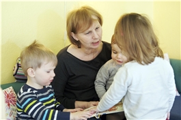 Eine Erzieherin betrachtet mit mehreren kleinen Kindern ein Bilderbuch / D. Wäsche
