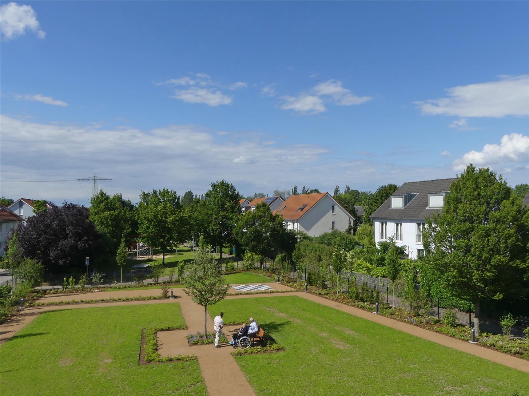 Blick von oben auf die Gartenanlage von Haus Raphael mit Wiese, Wegen, Ruhebank, Sträuchern und frisch angelegten Blumenrabatten. (Foto: © Caritas Offenbach / Sabine Schilha)