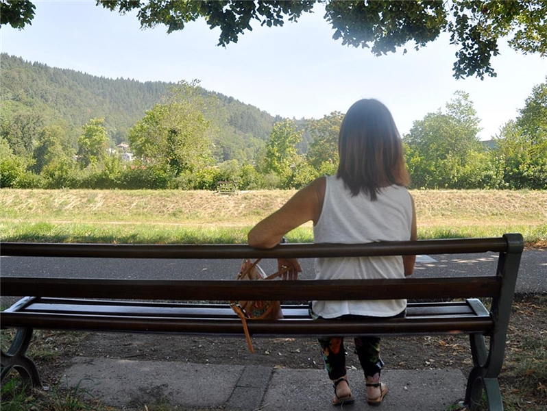 Von hinten zu sehende Frau sitzt auf eine Bank in freier Natur