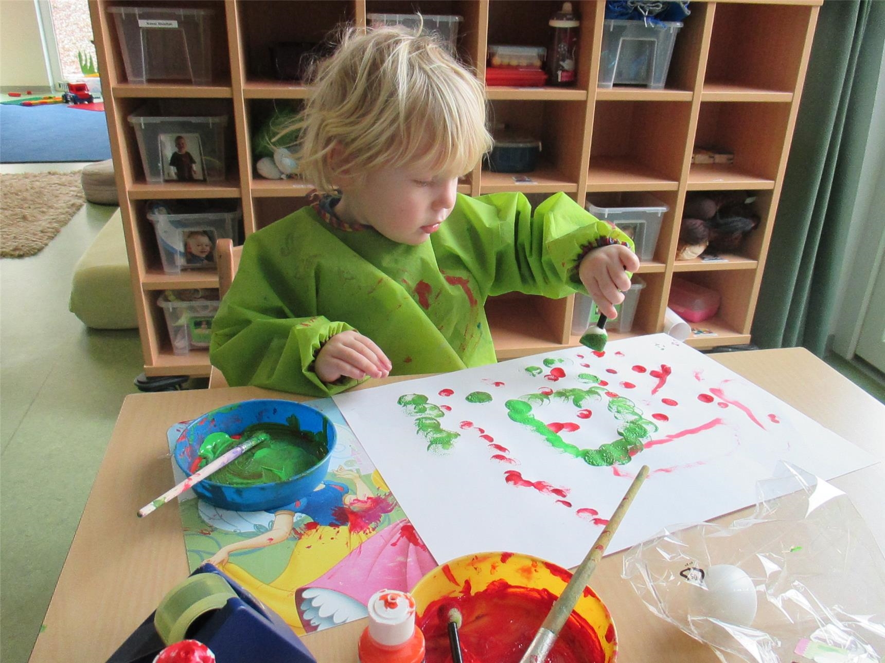 Ein Kind sitzt an einem Tisch und stempelt Farbe auf ein Blatt Papier (Caritasverband Trier e. V.)