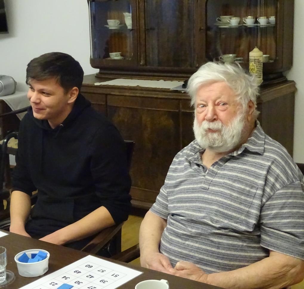 Junger Mann sitzt neben einem Senior mit weißem Bart am Tisch und spielen Bingo (Seniorenzentrum St. Bonifatius)