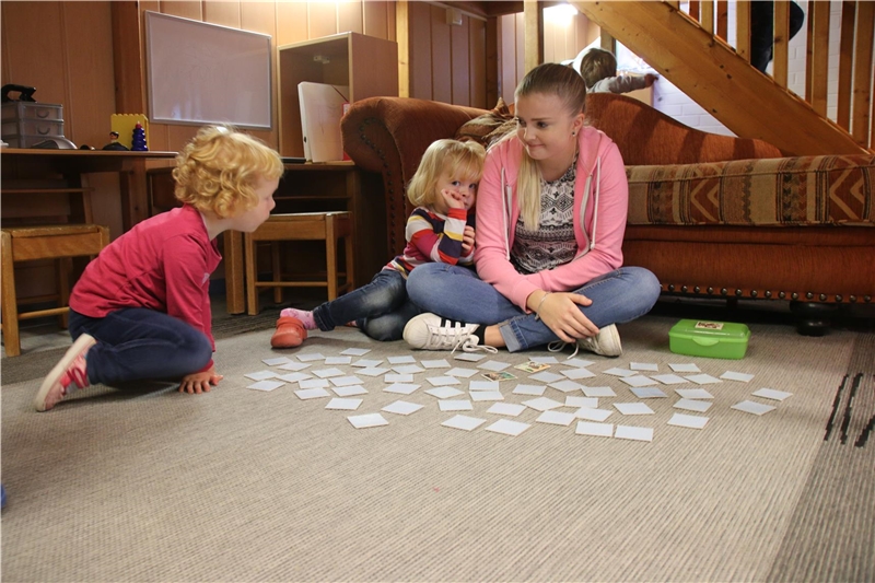 Das Foto zeigt zwei Kinder, die mit einer Erzieherin vor Spielzelt spielen.