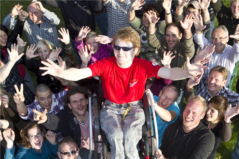 jubelnde Gruppe Menschen hebt Mann im Rollstuhl in die Luft (©caritasverband bocholt)
