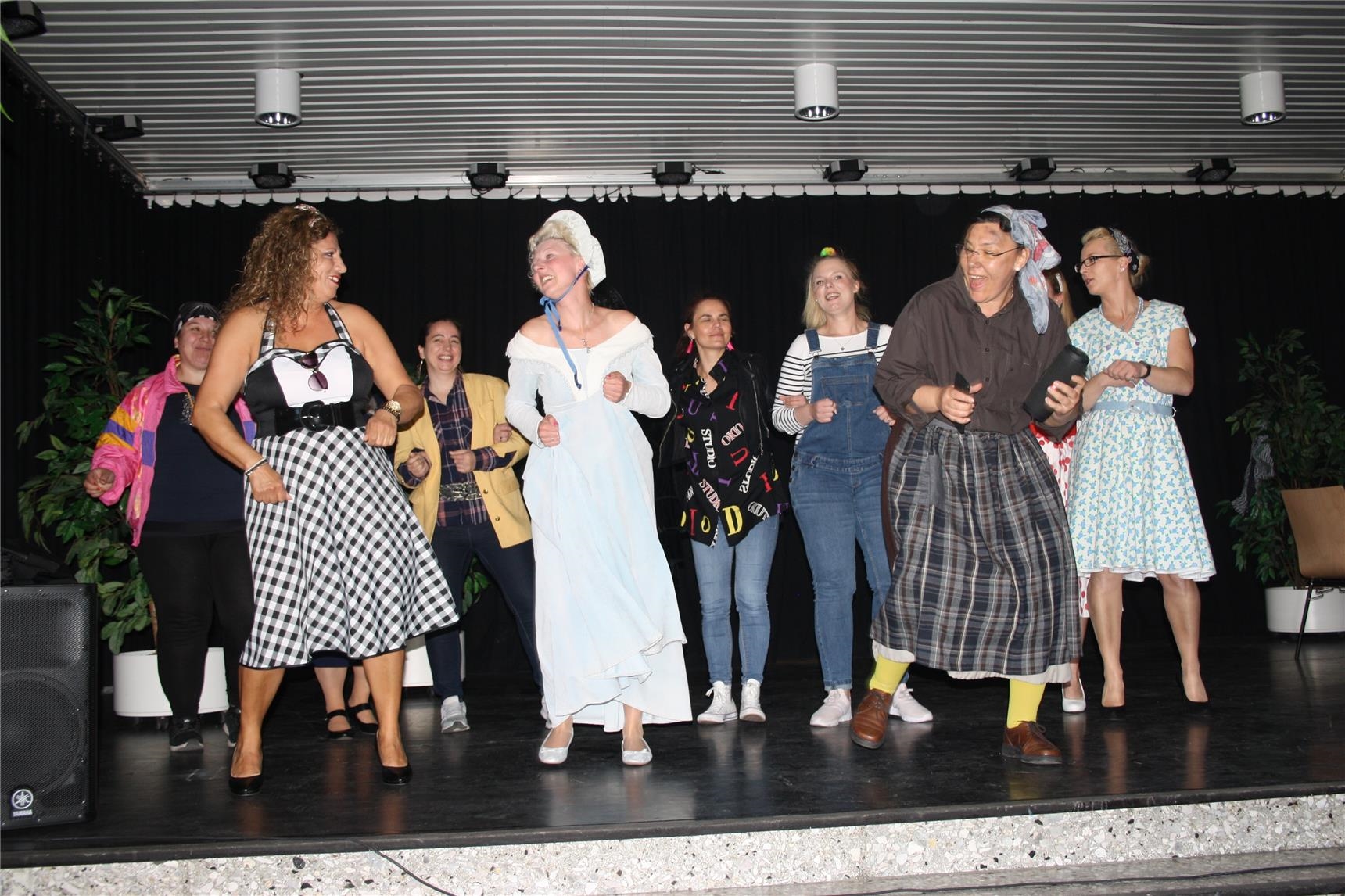 Neun Frauen in der Kleidung verschiedener Jahrzehnte tanzen auf der Bühne (Caritas Hamm)