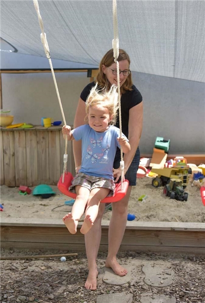 Das Foto zeigt eine Mutter, die ihrem Kind auf einer Schaukel Anschwung gibt.