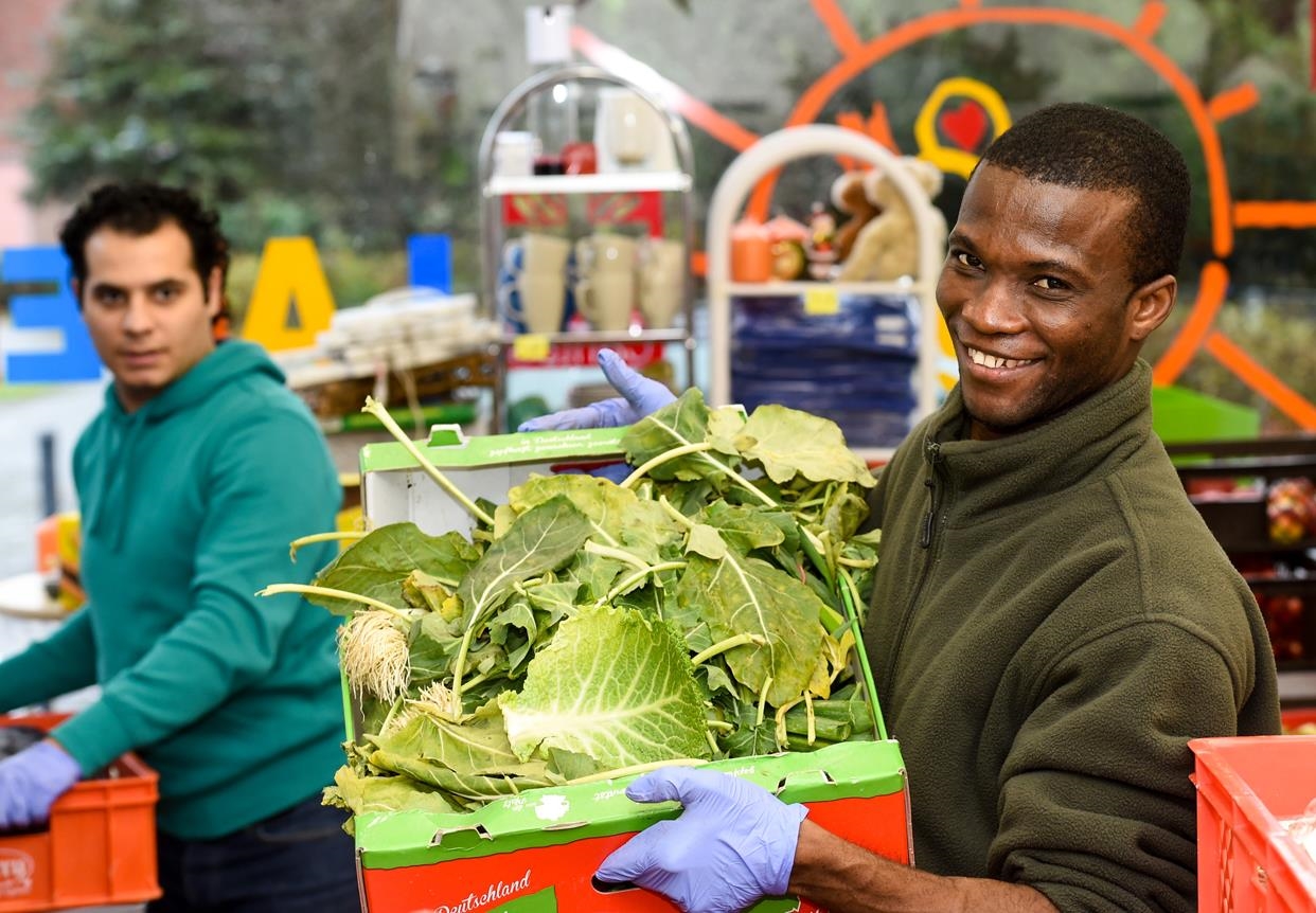 Zwei Flüchtlinge tragen Gemüsekisten (DCV / KNA)