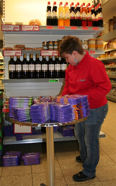 Eine Verkäuferin stapelt Schokoladentafeln auf eine silbernen Tisch, der vor einem Warenregal steht (Markus Lahrmann)