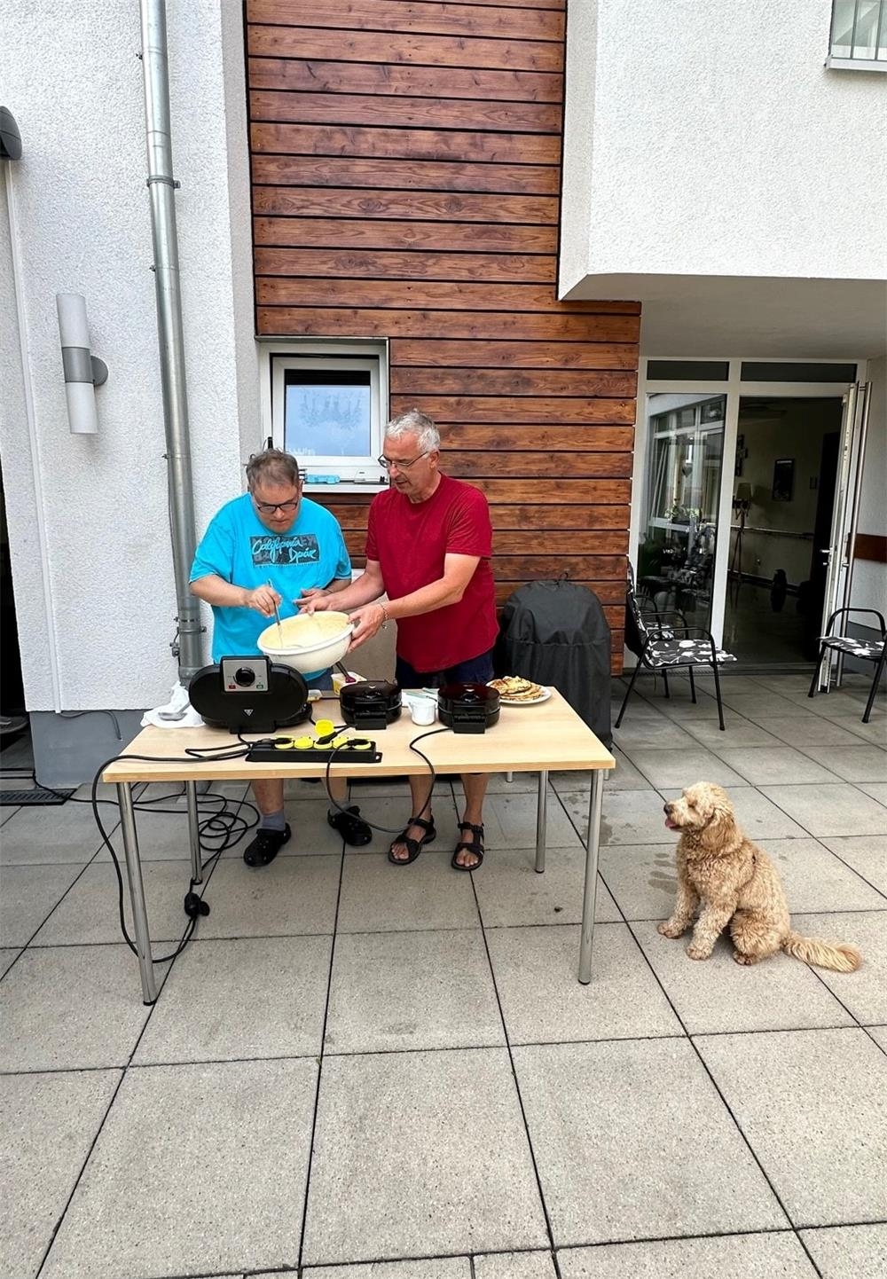 Zwei Personen stehen hinter einem Tisch mit Waffeleisen und backen. 