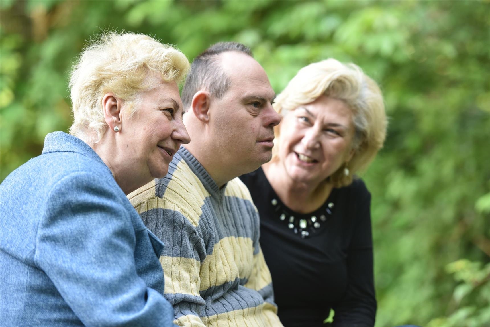 Zwei Schwestern sprechen mit ihrem Bruder mit Behinderung auf einer Parkbank