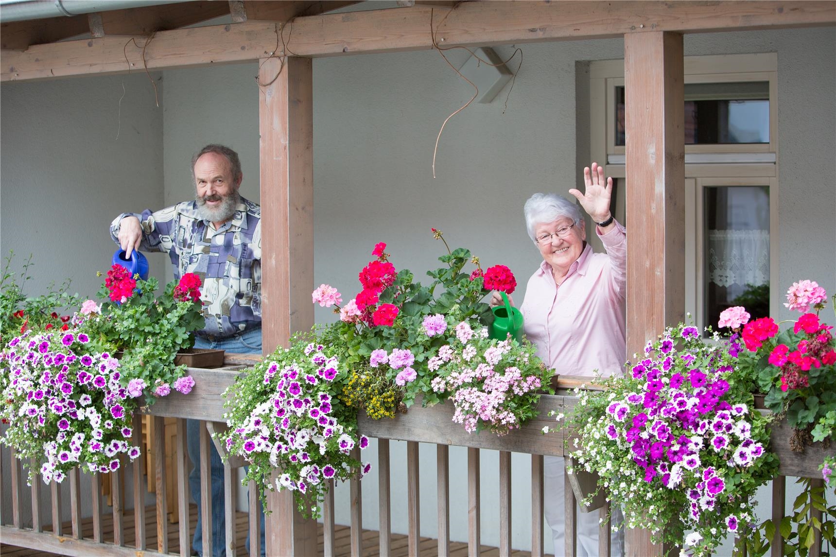 zwei Bewohner auf Balkon beim Blumen gießen 