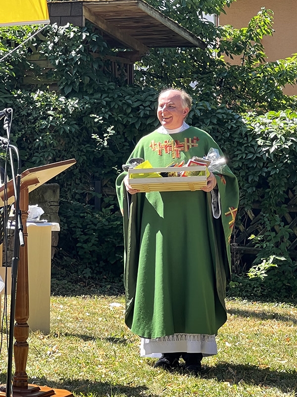 Ein Pfarrer hält einen Kasten mit Geschenken an ihn und freut sich (Caritasverband Darmstadt e. V. / Jens Berger)