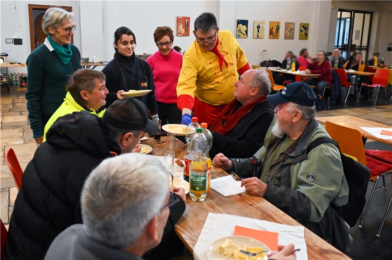 Küchenmeister Sebastian Küpper serviert in der Caritaskirche einer Gruppe von wohnungslosen Menschen das von ihm gekochte Essen.