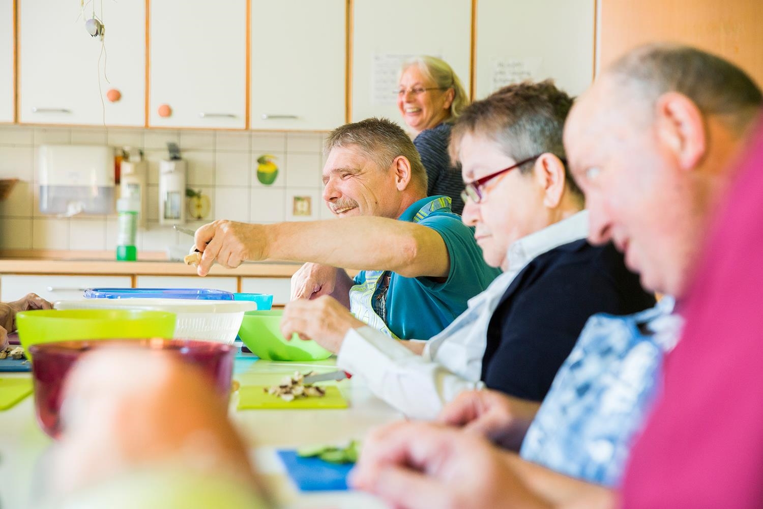 Mehrere Menschen mit Behinderung schneiden am Tisch Gemüse und lachen dabei (Deutscher Caritasverband e. V. / Sebastian Pfütze)